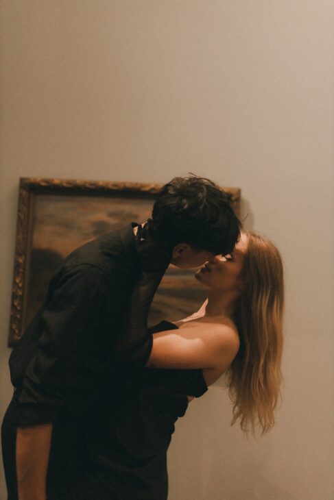 a man and a woman kissing in front of a painting