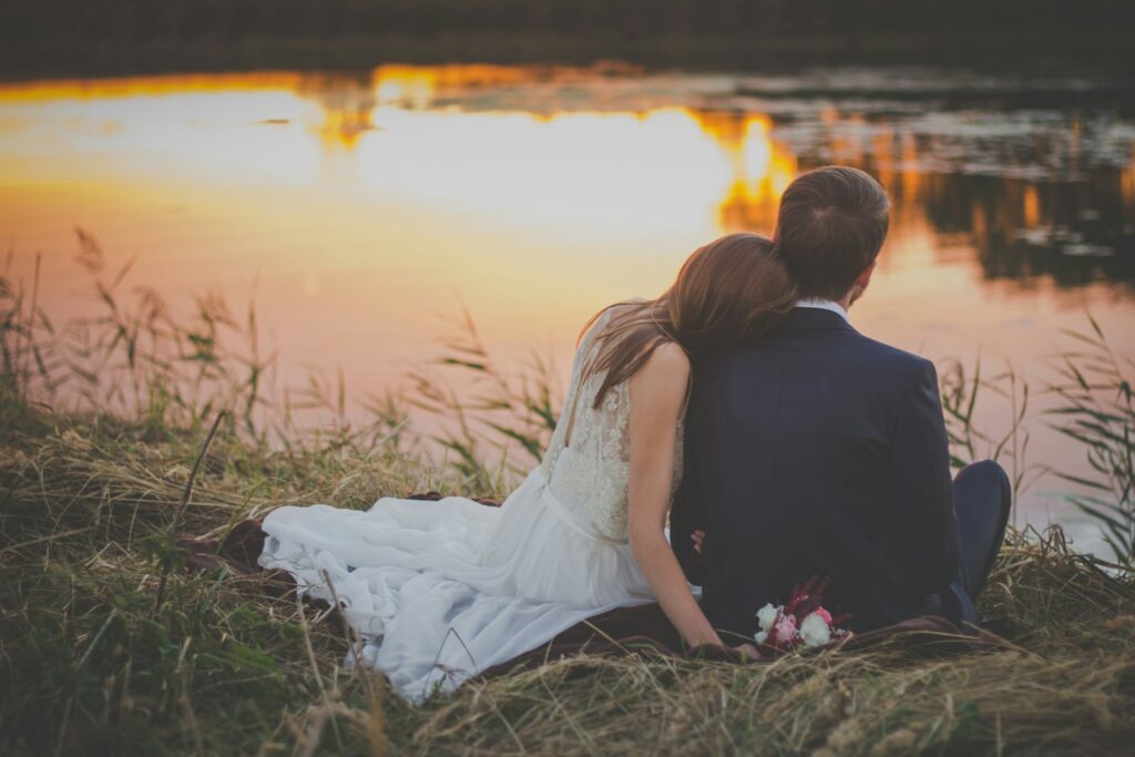 sitting woman leaning on man's shoulder facing lake during golden hour - Happily Ever After
