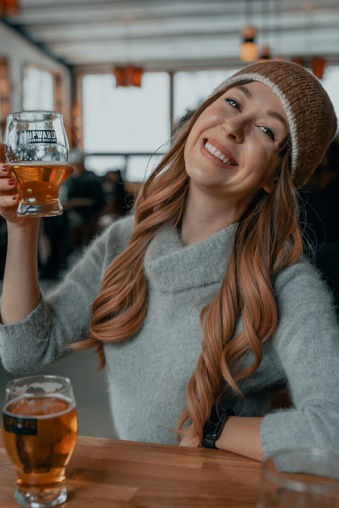 smiling woman in gray sweater holding clear drinking glass with brown liquid