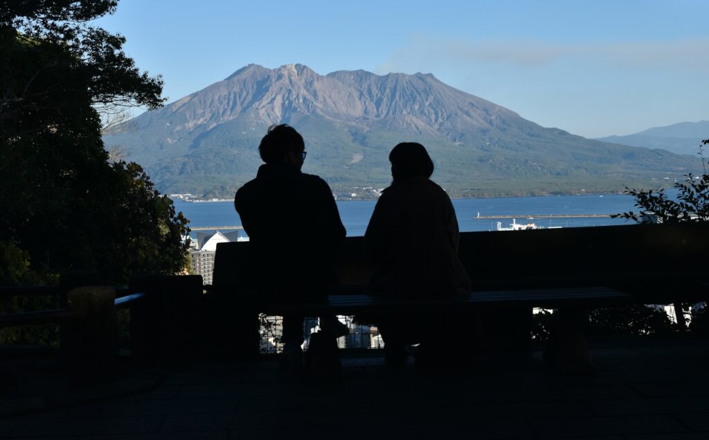 two people sitting on a bench looking at a mountain