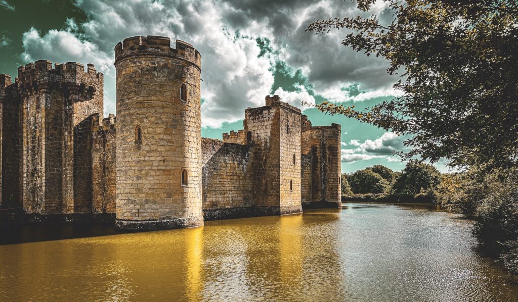 a castle sitting on top of a river next to a forest Bodiam Castle