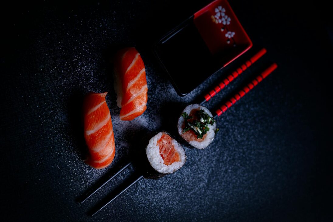 A vibrant display of salmon sushi and maki rolls with chopsticks and soy sauce, shot from above.