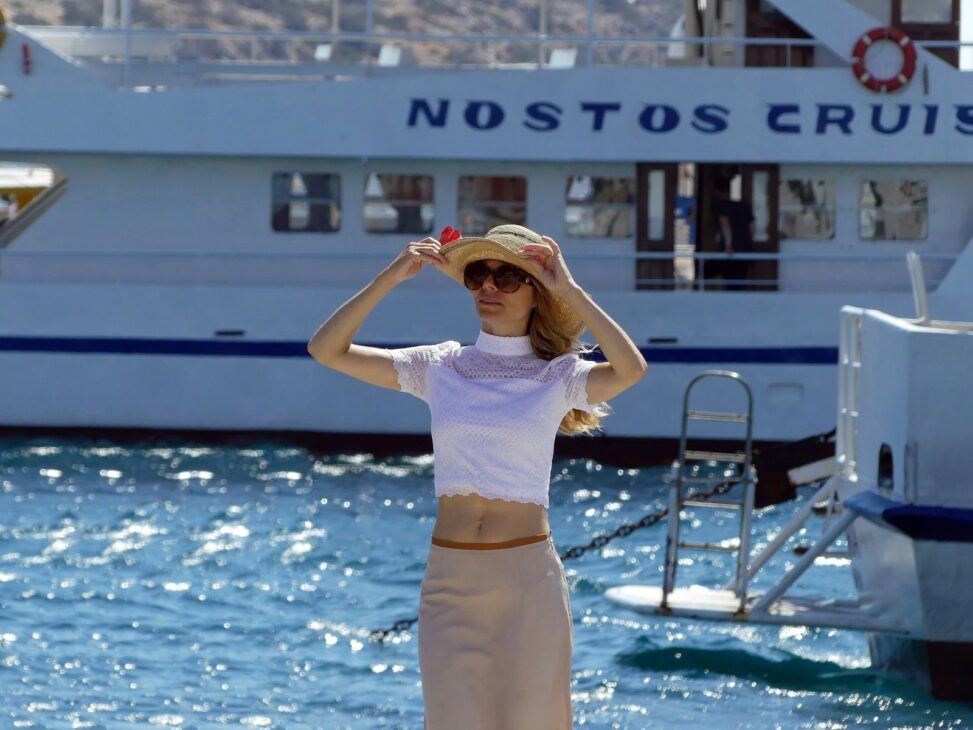 a woman in a skirt and a hat standing in front of a boat