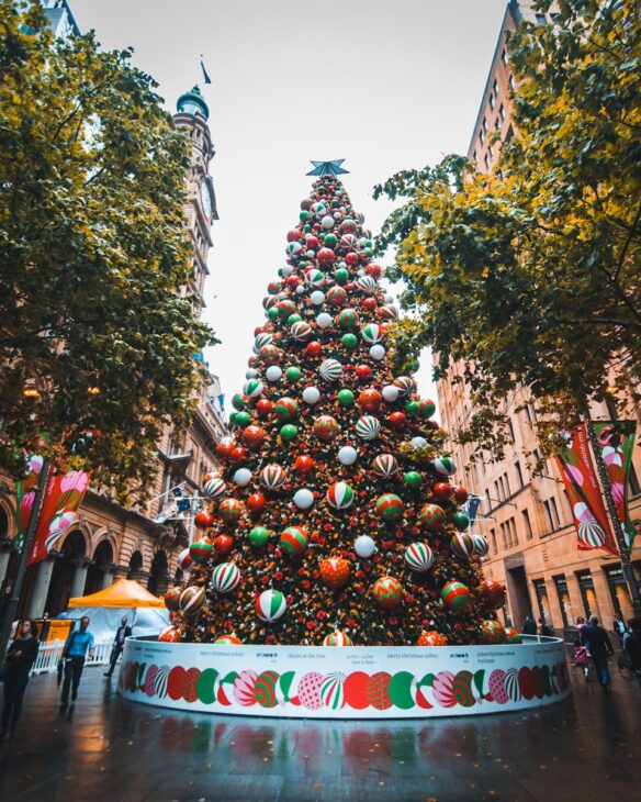 people walking beside Christmas baubles on large tree
